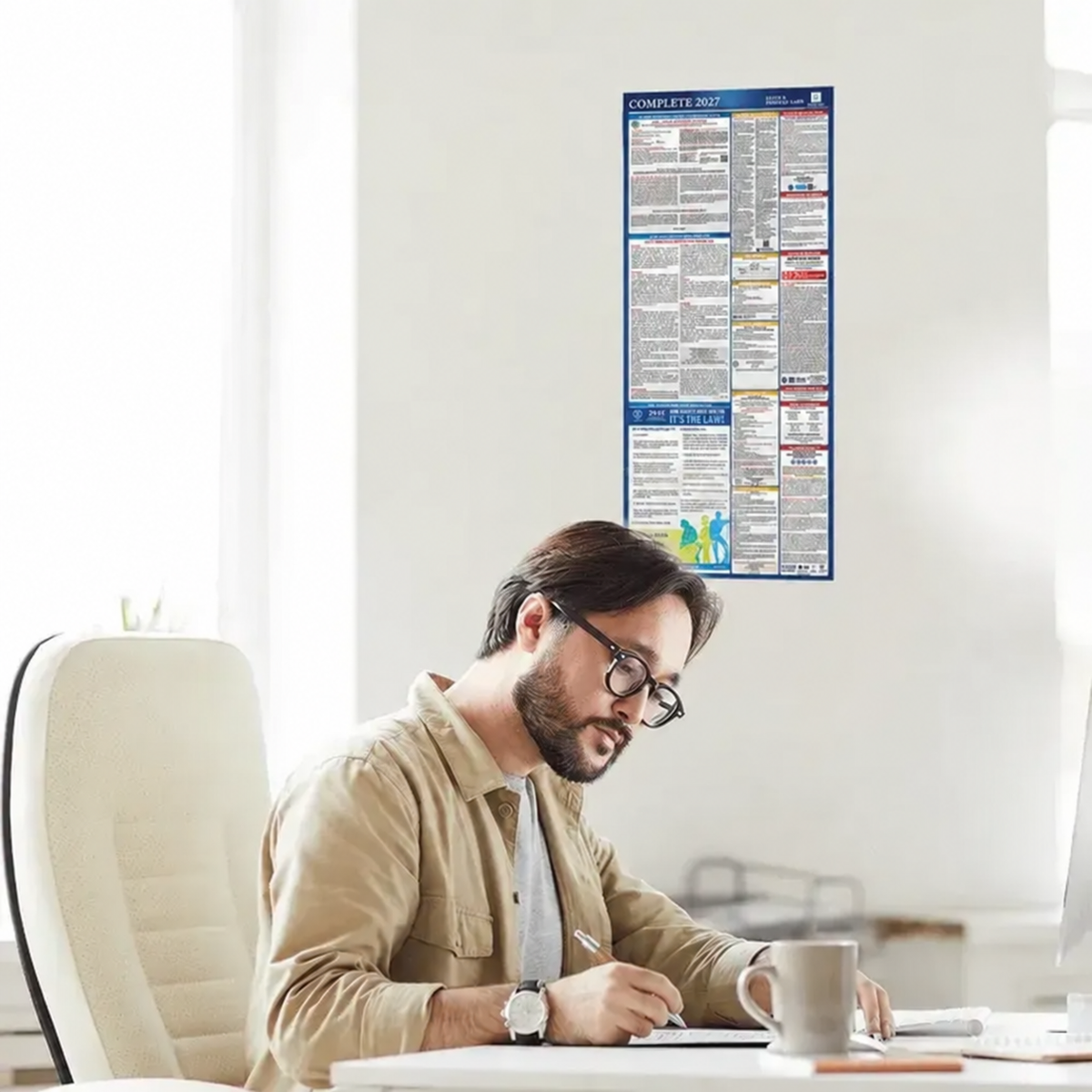 Employee working at a desk beneath a complete 2027 all-in-one state and federal labor law poster on the office wall